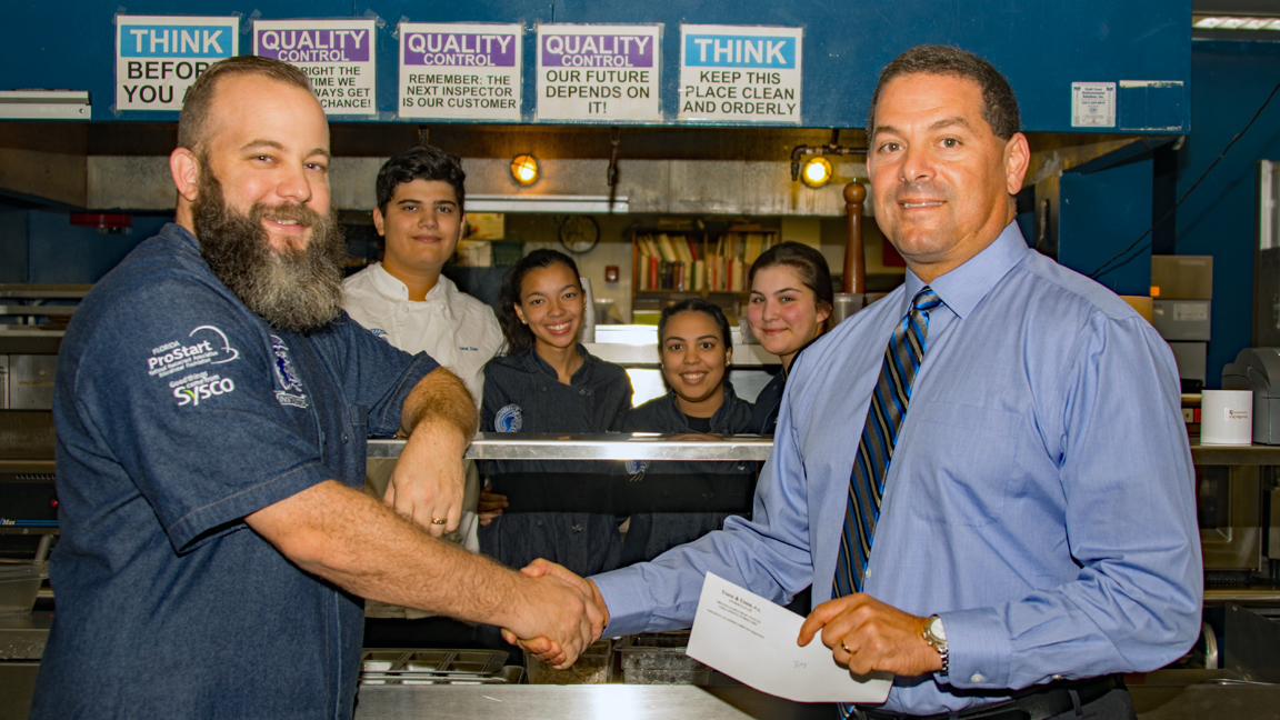 Scott Goodman, Culinary & Hospitality Instructor receives a check from Broward County Commissioner Michael Udine.